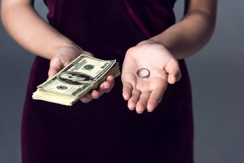 cropped shot of woman holding stack of cash and wedding ring, marriage of convenience concept