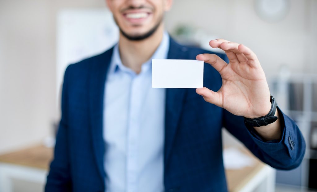 Cropped view of young Arab man showing empty business card with mockup for design at modern office