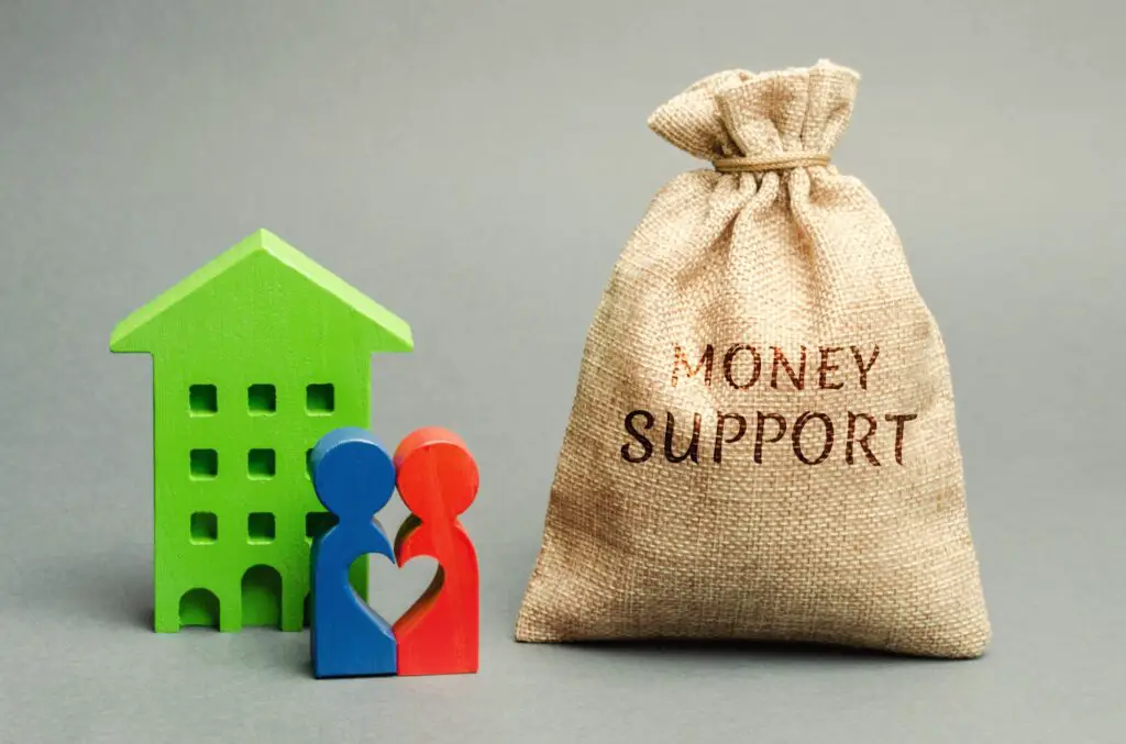 Family standing near the house with a bag with the word Money support