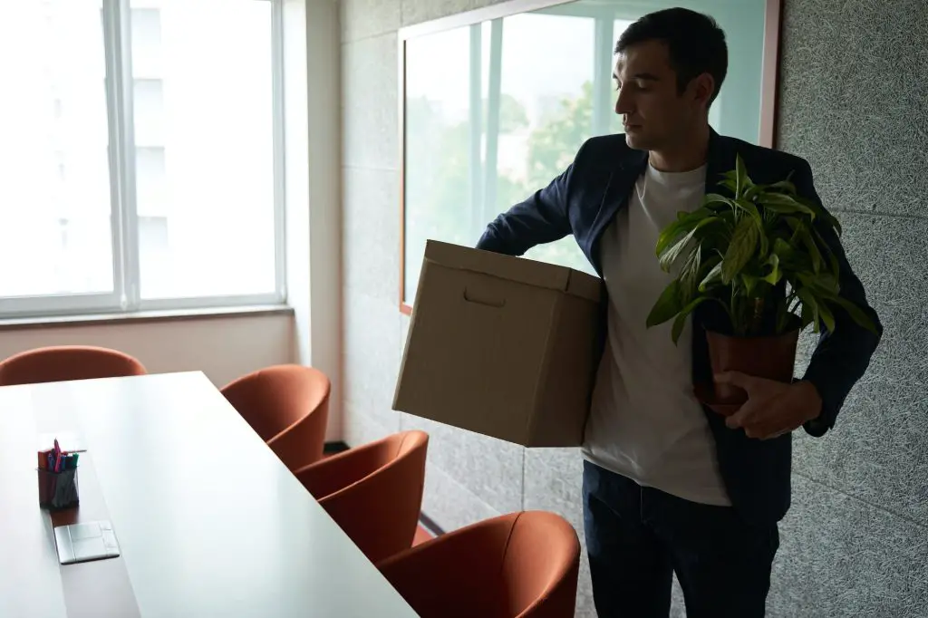 Fired worker carrying box with belongings and plant