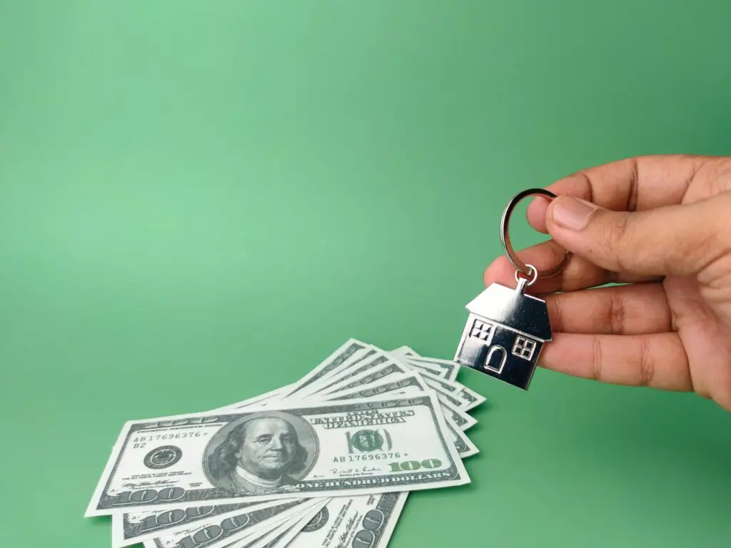 Hand holding house keychain and banknotes on a green background with copy space.Home buying concept