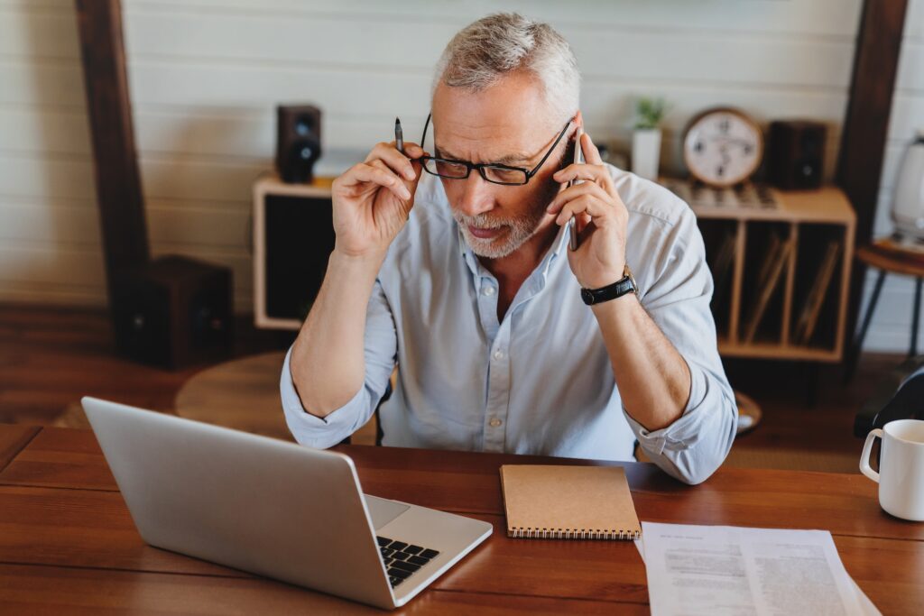 Senior man checking home finances or bank account while talking on mobile phone