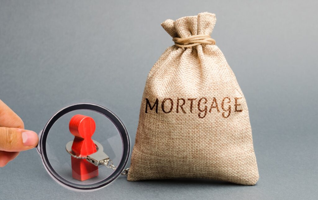 The figure of a man is handcuffed to a money bag with the word Mortgage