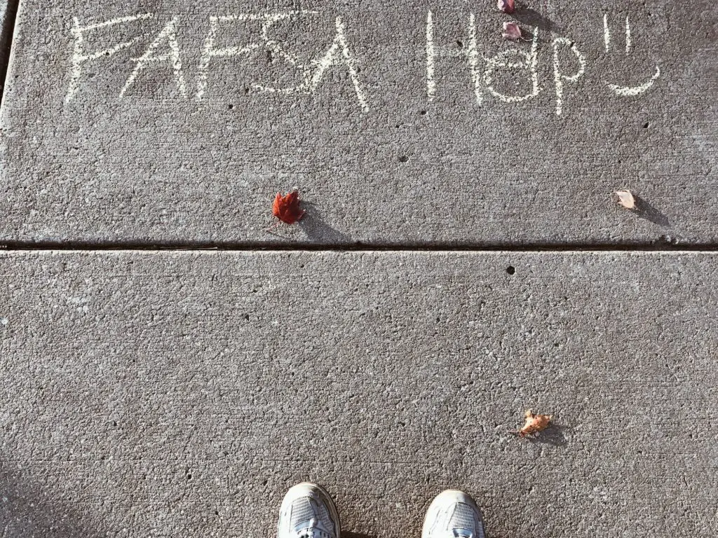 College student looking down at words on sidewalk written in chalk with message for FAFSA help