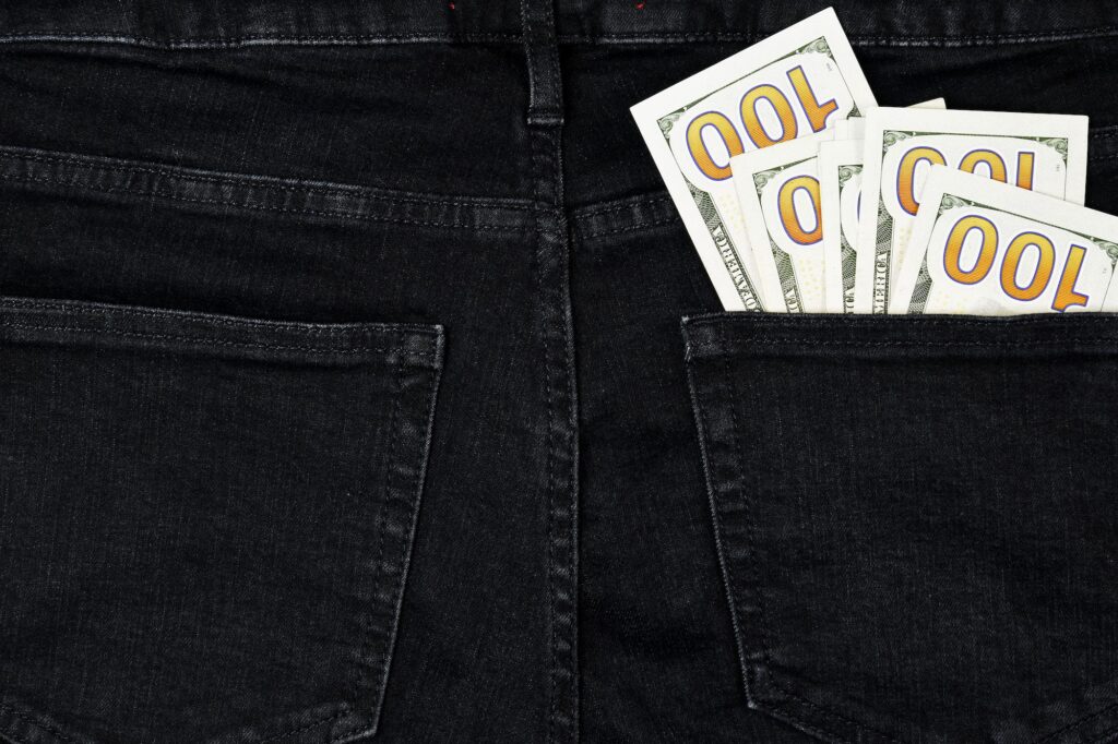 Stack of hundred dollar bills in back pocket of black jeans, denim background texture. Spending Mone